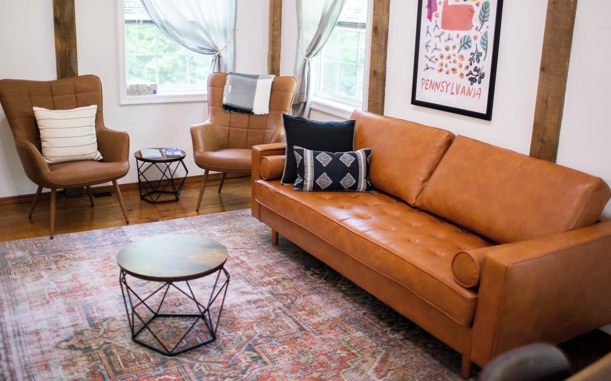 Un salon avec un canapé en cuir marron, deux fauteuils, une petite table ronde et un tapis à motifs.