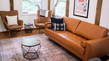 Un salon avec un canapé en cuir marron, deux fauteuils, une petite table ronde et un tapis à motifs.