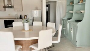 Una cocina moderna con armarios blancos, una mesa de comedor con sillas blancas y un mueble azul claro con estantes.
