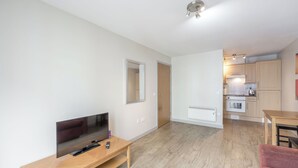 A modern apartment with a TV on a wooden stand, a kitchen with wooden cabinets, and a red chair. - Central 1 BR apartment in Birmingham (Birmingham)