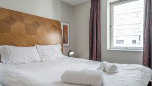 A hotel room with a large bed, a wooden headboard, a window with curtains, and a wall-mounted lamp. - Central 1 BR apartment in Birmingham (Birmingham)