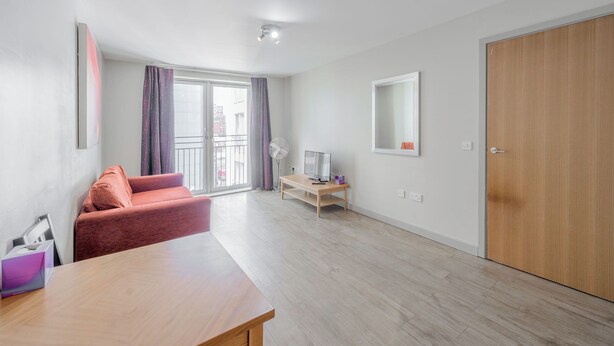 A modern living room with a sofa, a TV on a wooden stand, a sliding glass door to the outside, and a wooden wardrobe. - Central 1 BR apartment in Birmingham (Birmingham)