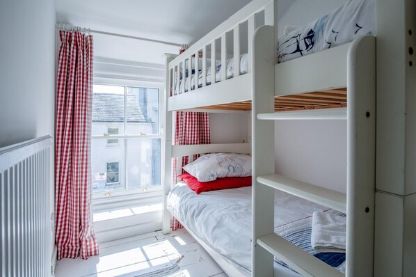 A bunk bed room with a window, white walls, and red and white checkered curtains.