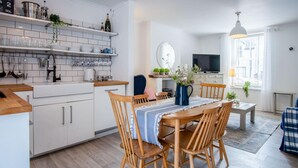 Una cucina moderna con mobili bianchi, un tavolo da pranzo in legno e una TV nella zona living.