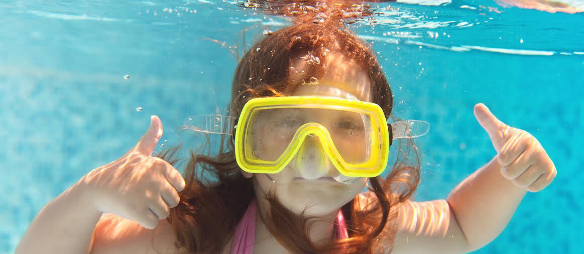 A person underwater in a pool with clear blue water.