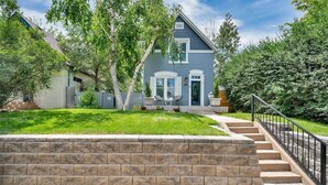 Una casa de dos pisos con un muro de contención de piedra, un porche con mobiliario exterior y una escalera que conduce a la puerta principal.