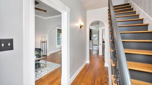 Un pasillo con suelo de madera, paredes blancas y una escalera de madera con barandilla de metal.