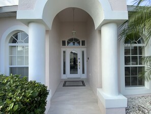 A building entrance with a white facade, arched doorways, and a central entrance with a glass door.
