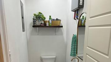 A compact bathroom with a toilet, sink, and a small shelf with toiletries.