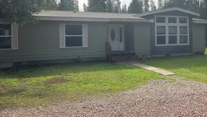 Ein eingeschossiges Haus mit Veranda, einer kleinen angeschlossenen Garage und einem Rasen.