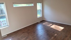 Ein Zimmer mit Holzboden, zwei Fenstern und einer weißen Wand.