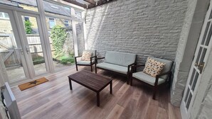 A sunlit room with a stone wall, wooden flooring, and a sofa set with patterned cushions. - Brylie House, Large Central Family Home (Skipton)