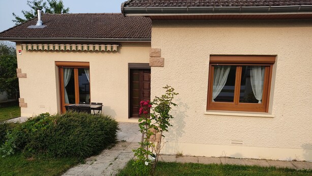 Ein zweistöckiges Haus mit einem gepflasterten Weg, der zu einer Holztür und einem Fenster mit Vorhängen führt.