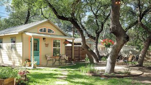 A small, single-story house with a front porch, a small garden, and a tree in the yard. - Romantic~Butterfly Cttg~Central Loc, Firepit ~Oaks (San Antonio)