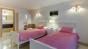 Une chambre avec deux lits, une armoire, une chaise et une table de chevet avec une lampe.