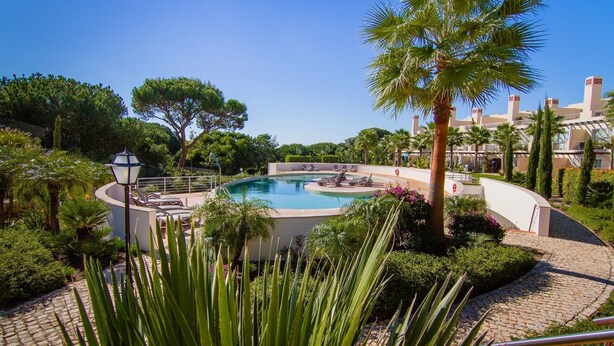 Une piscine entourée de palmiers et de chaises longues, avec un ciel bleu azur en arrière-plan.