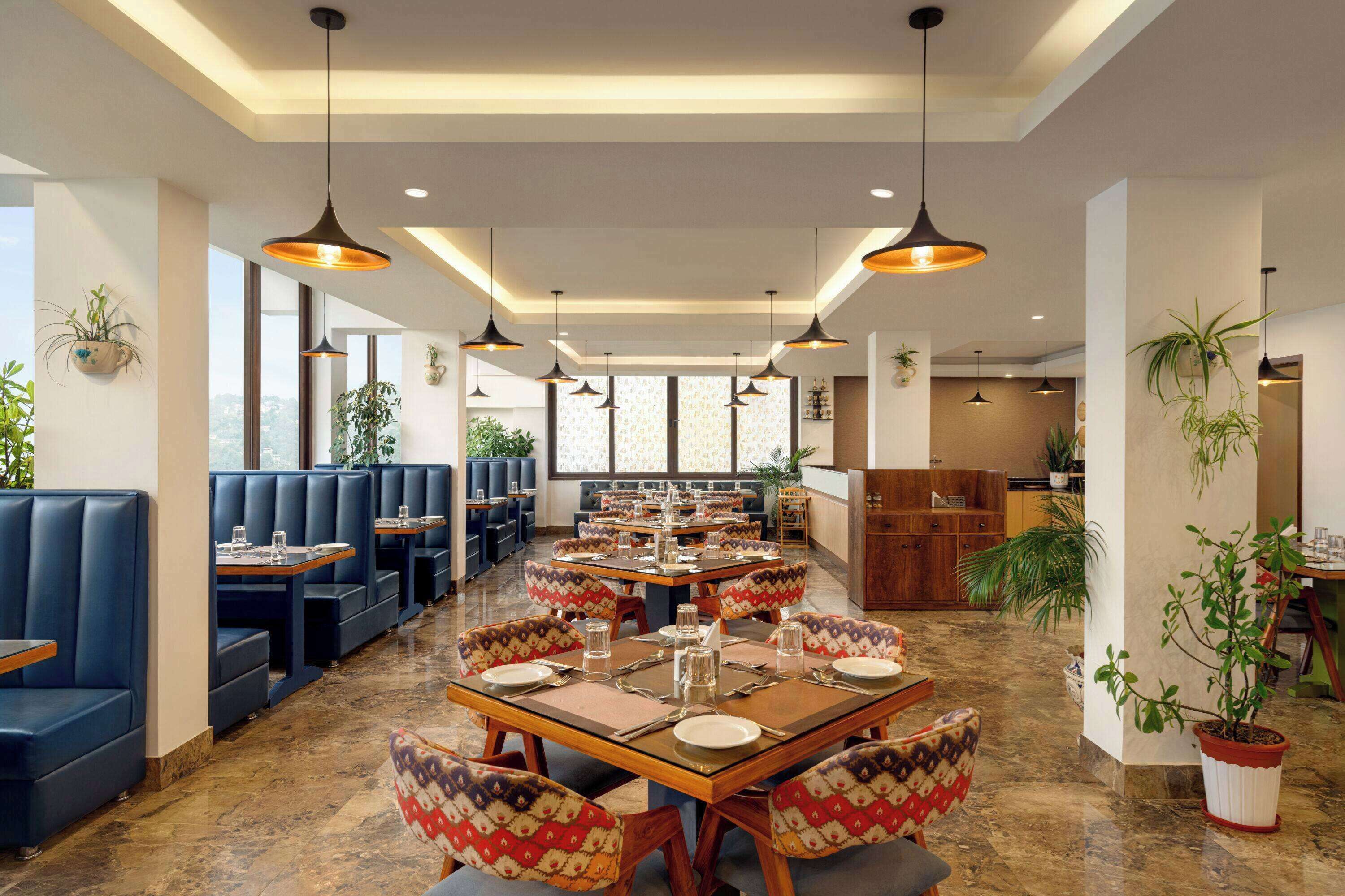 Un restaurante con cabinas y mesas, suelo de madera, lámparas colgantes y plantas en macetas.