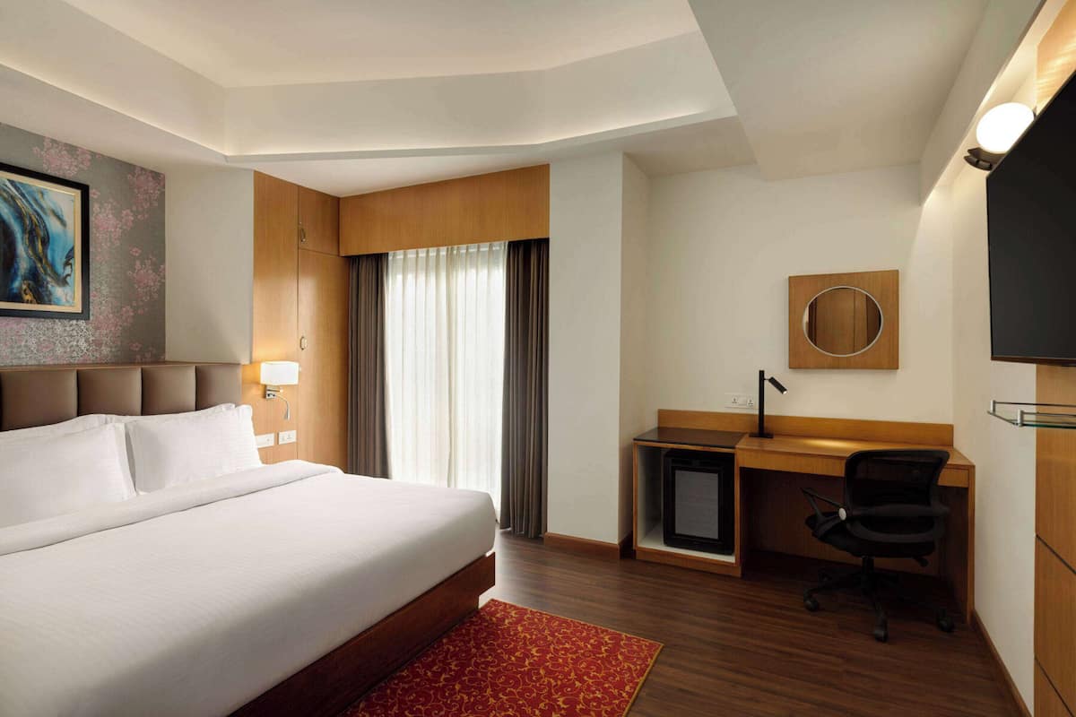 Une chambre d’hôtel avec un grand lit, un bureau avec une chaise, une télévision et un grand miroir rond fixé au mur.
