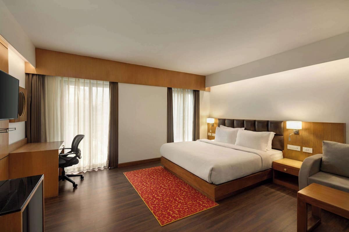 Une chambre d’hôtel avec un grand lit, un bureau, une chaise, une télévision et un tapis rouge.