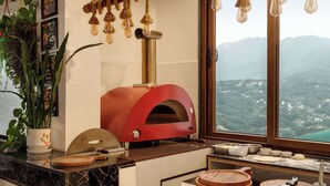 A kitchen with a red pizza oven, a large window with a mountain view, and various cooking utensils on the counter. - Days Inn By Wyndham Gangtok Tadong (Gangtok)