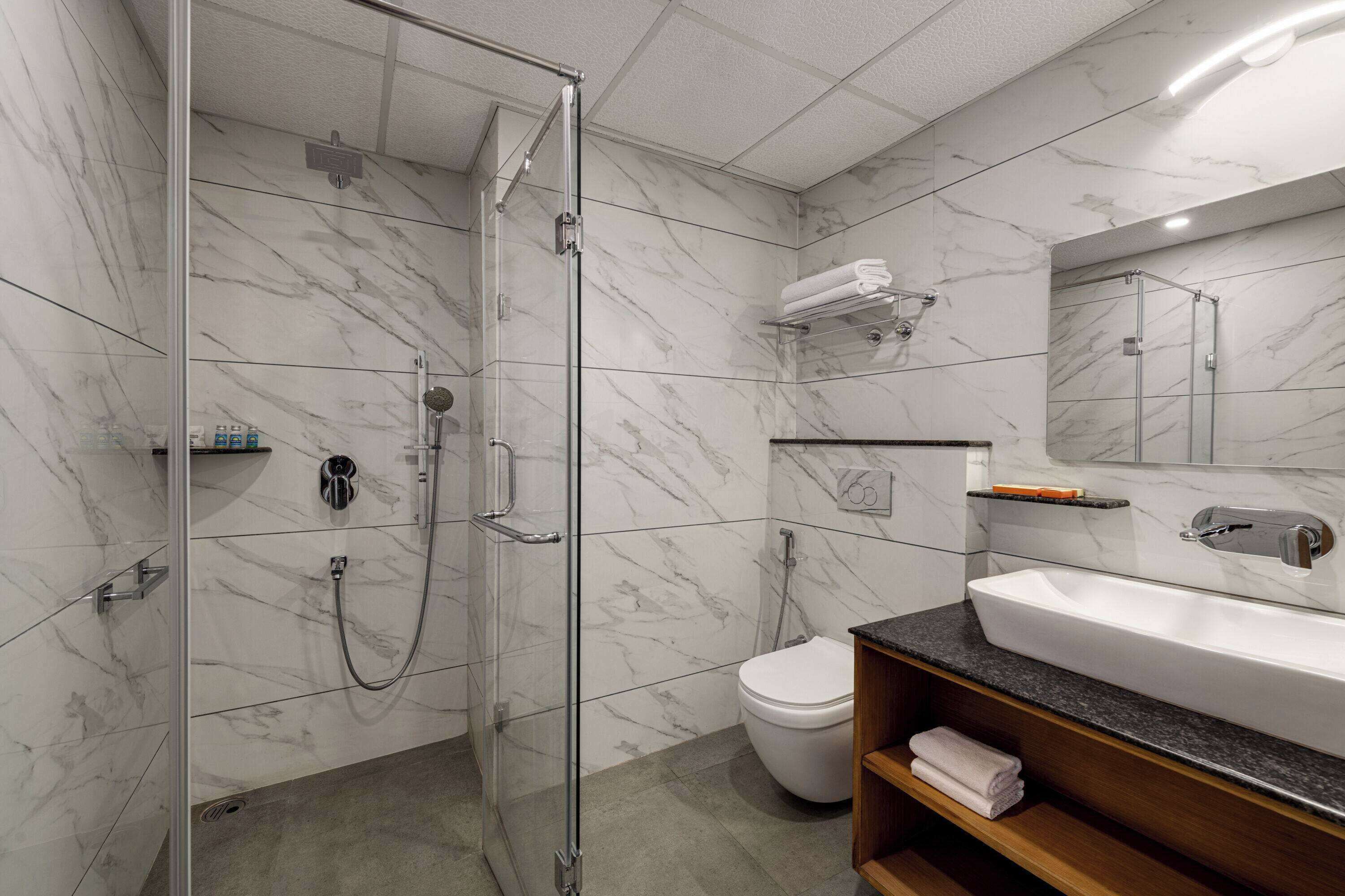 Een moderne badkamer met een glazen douchecabine, een wit toilet en een betegelde muur van marmer.