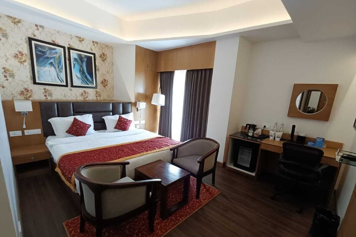 Une chambre d’hôtel avec un grand lit, un bureau avec une chaise, une petite table, une machine à café et un téléviseur.