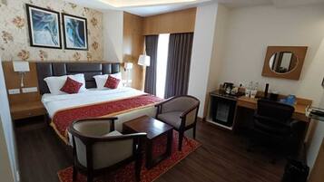 A hotel room with a large bed, a desk with a chair, a small table, a coffee machine, and a TV.