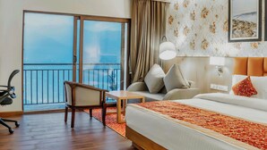 A hotel room with a large bed, a desk, a chair, a balcony with a view, and a wall with a floral pattern. - Days Inn By Wyndham Gangtok Tadong (Gangtok)