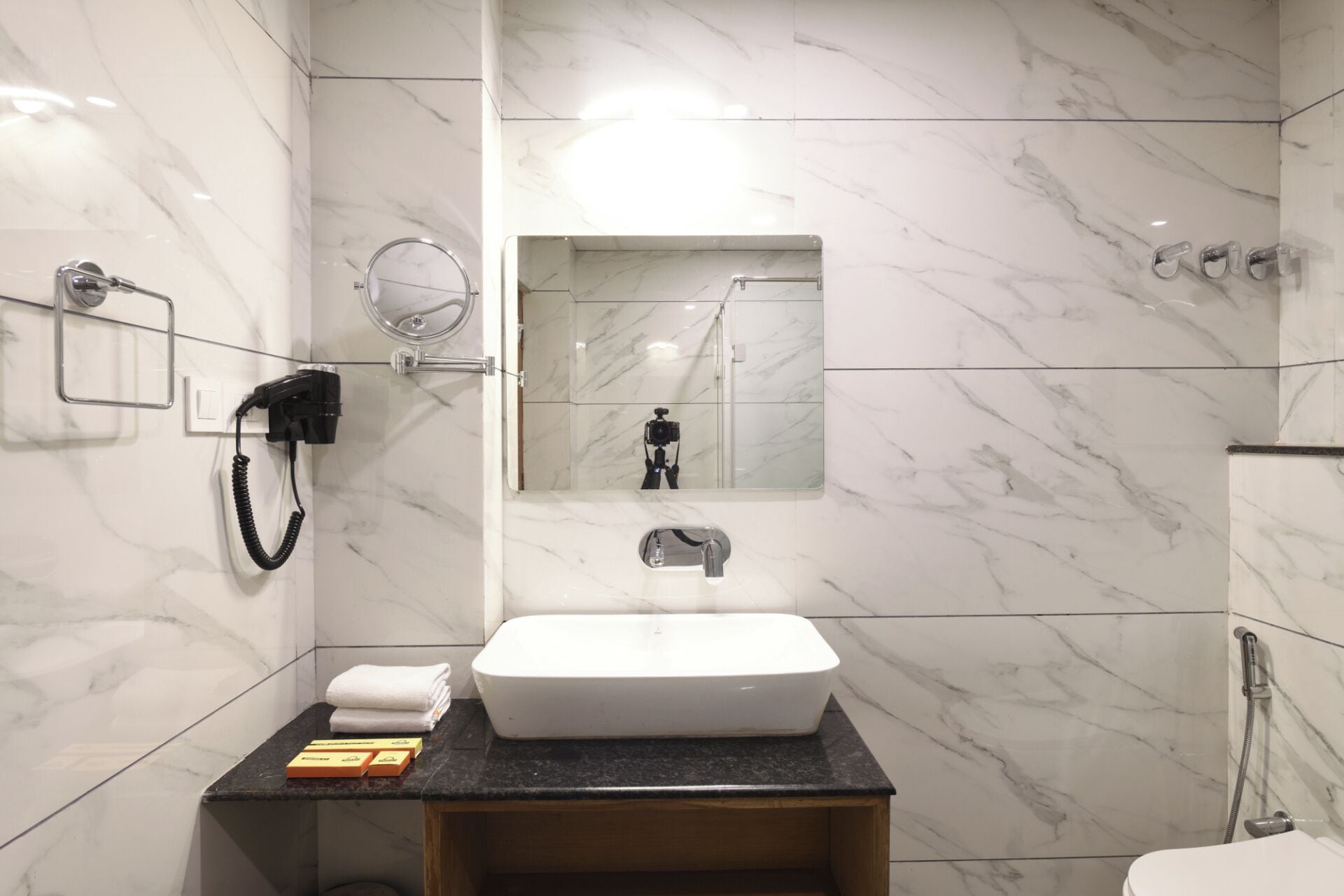 A modern bathroom with a white sink, marble walls, a mirror, and a shower.