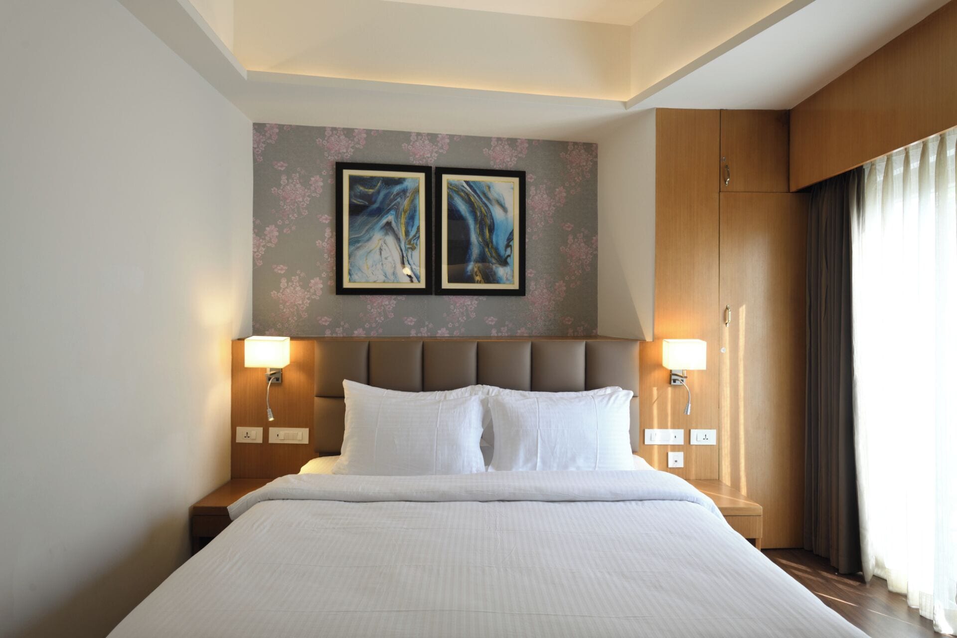 Ett hotellrum med en stor säng, två vägglampor och två inramade konstverk ovanför sängen.