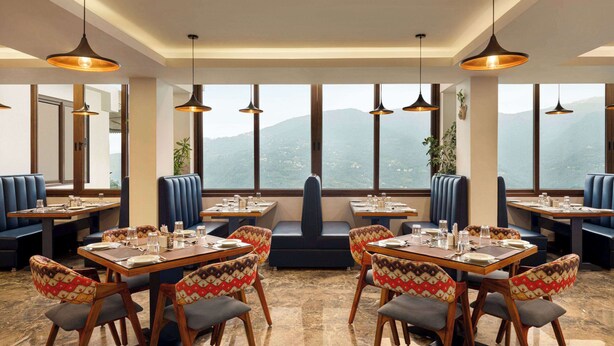 A restaurant with high tables and booths, large windows with a mountain view, and pendant lighting. - Days Inn By Wyndham Gangtok Tadong (Gangtok)