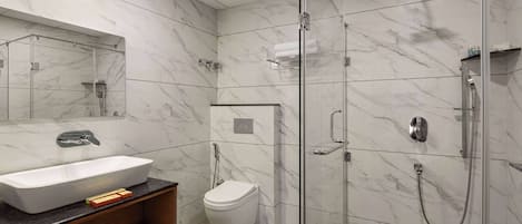 Un baño moderno con un lavamanos grande blanco, un inodoro y una zona de ducha con mampara de vidrio.
