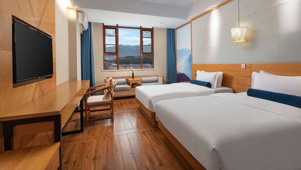 A hotel room with two beds, a desk, a chair, a TV, and a window with a mountain view.