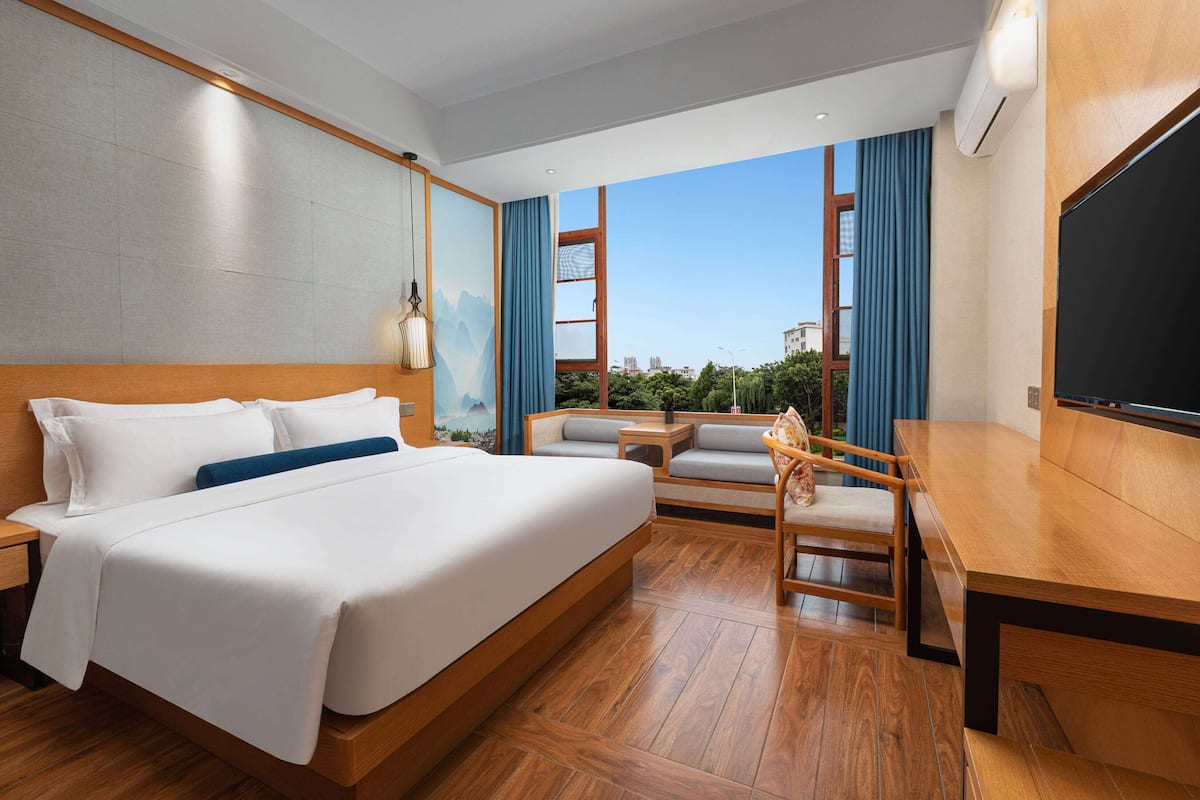 Ein Hotelzimmer mit einem großen Bett, einem Schreibtisch, einem Sessel und Blick auf die Stadt.