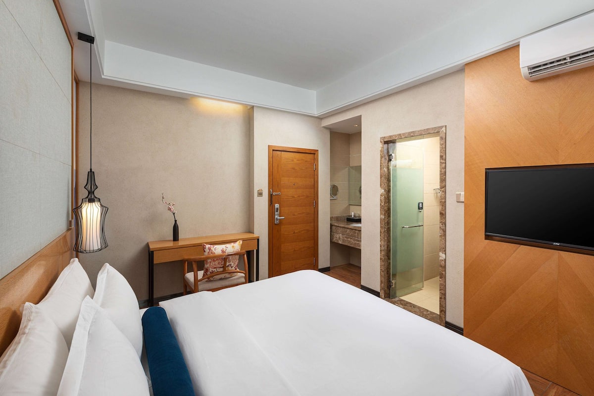 Ein Hotelzimmer mit Bett, Schreibtisch, Stuhl, Fernseher und einem durch eine offene Tür einsehbaren Badezimmer.