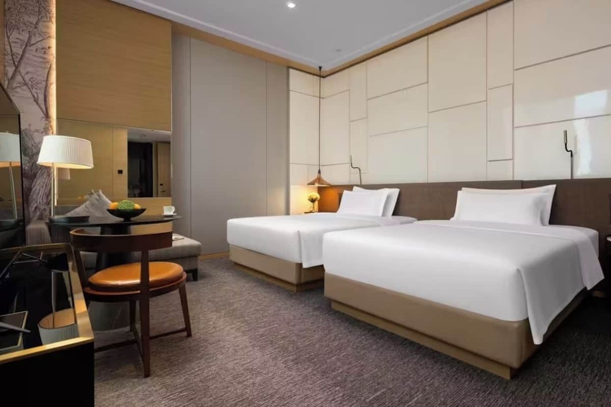 A hotel room with two beds, a desk with a chair, a lamp, and a mirror.
