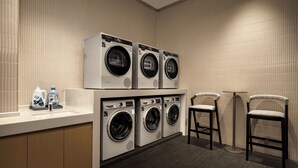 Une buanderie moderne avec des machines à laver superposées, un évier et deux chaises.