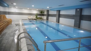 An indoor swimming pool with clear blue water, a wooden bench on the left, and a wall with a number '1.50'.