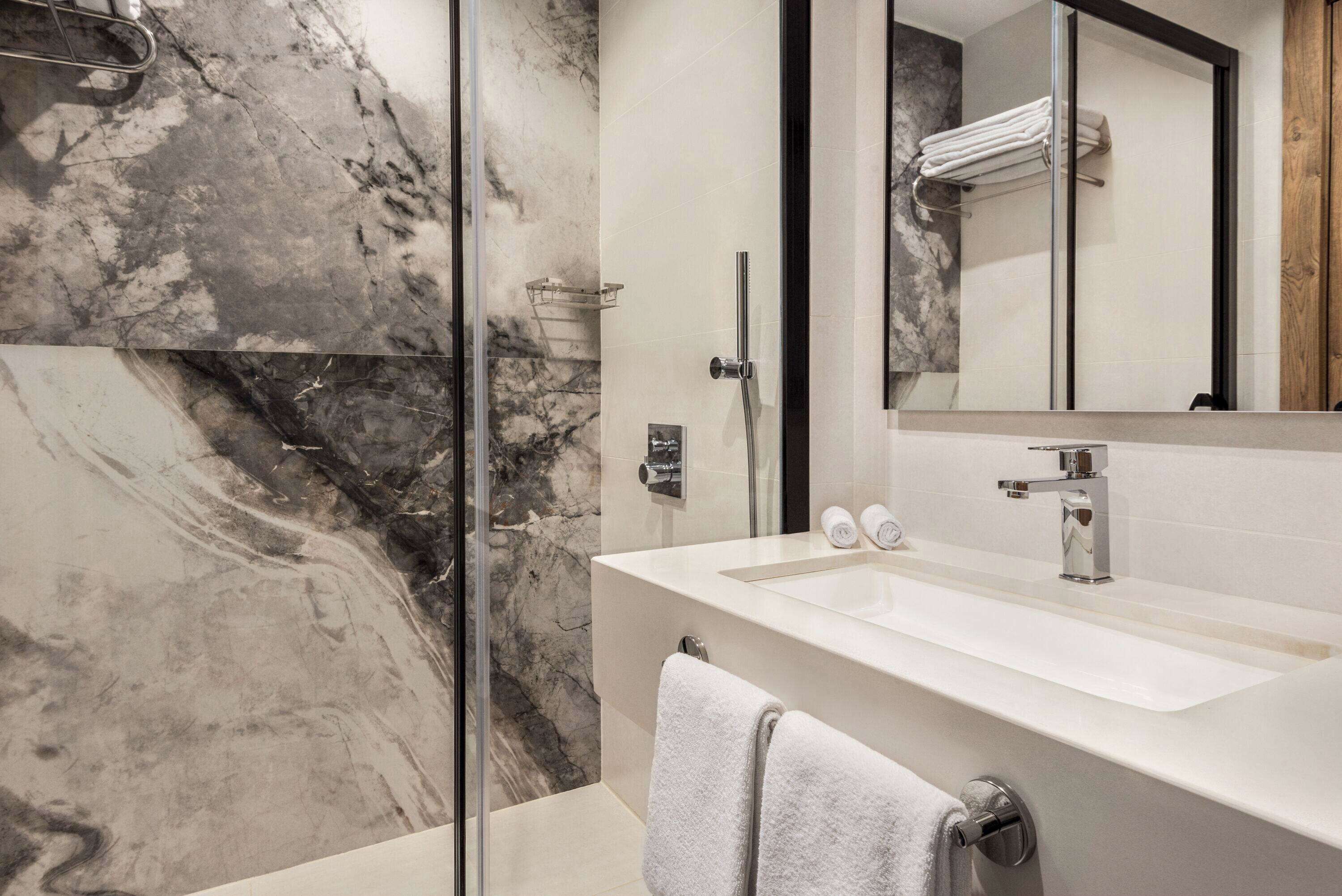 A modern bathroom with a glass shower enclosure, a white sink, and a large mirror.