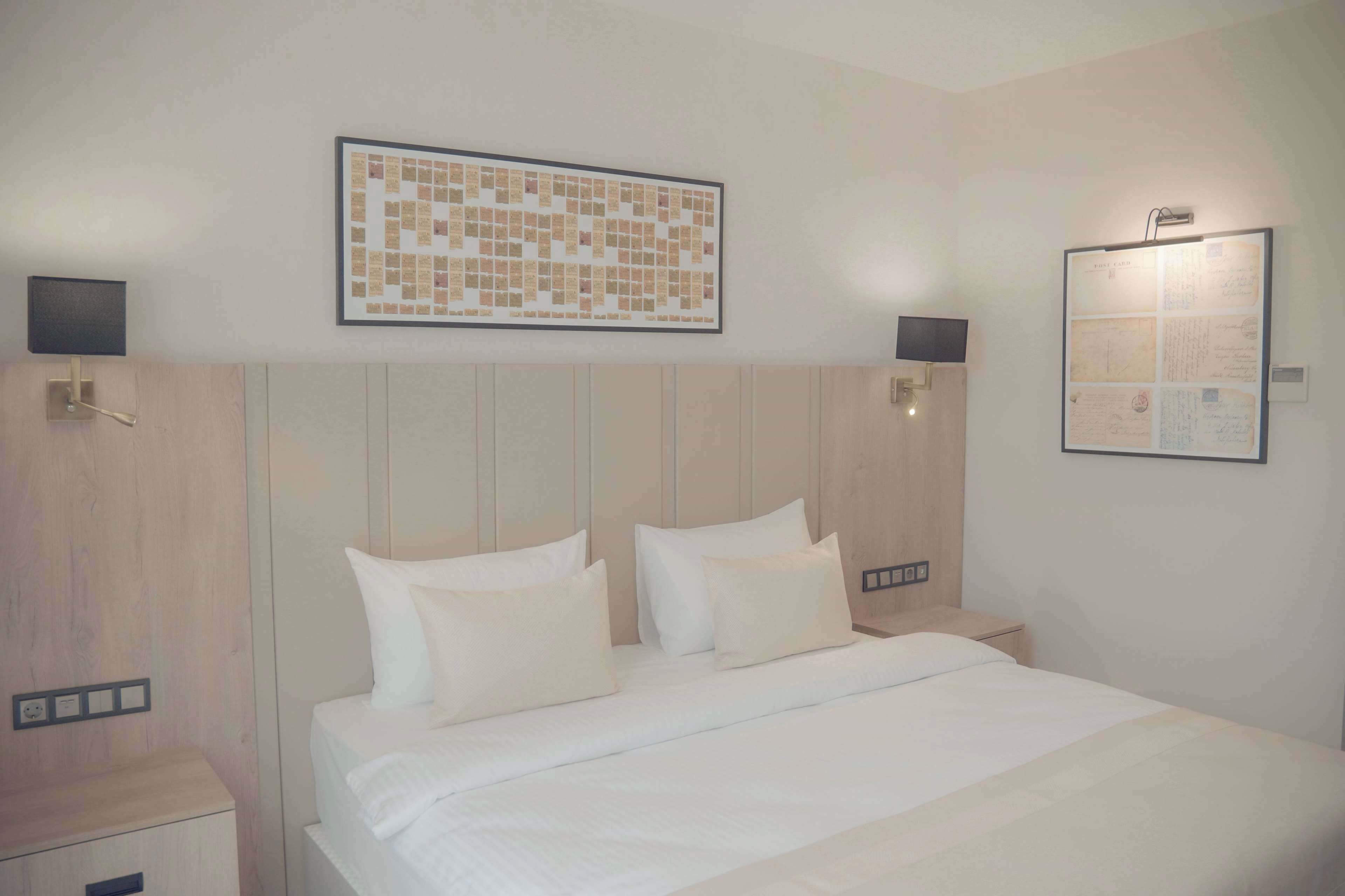 A hotel room with a large bed, two bedside tables, a wall-mounted light, and a framed artwork above the bed.