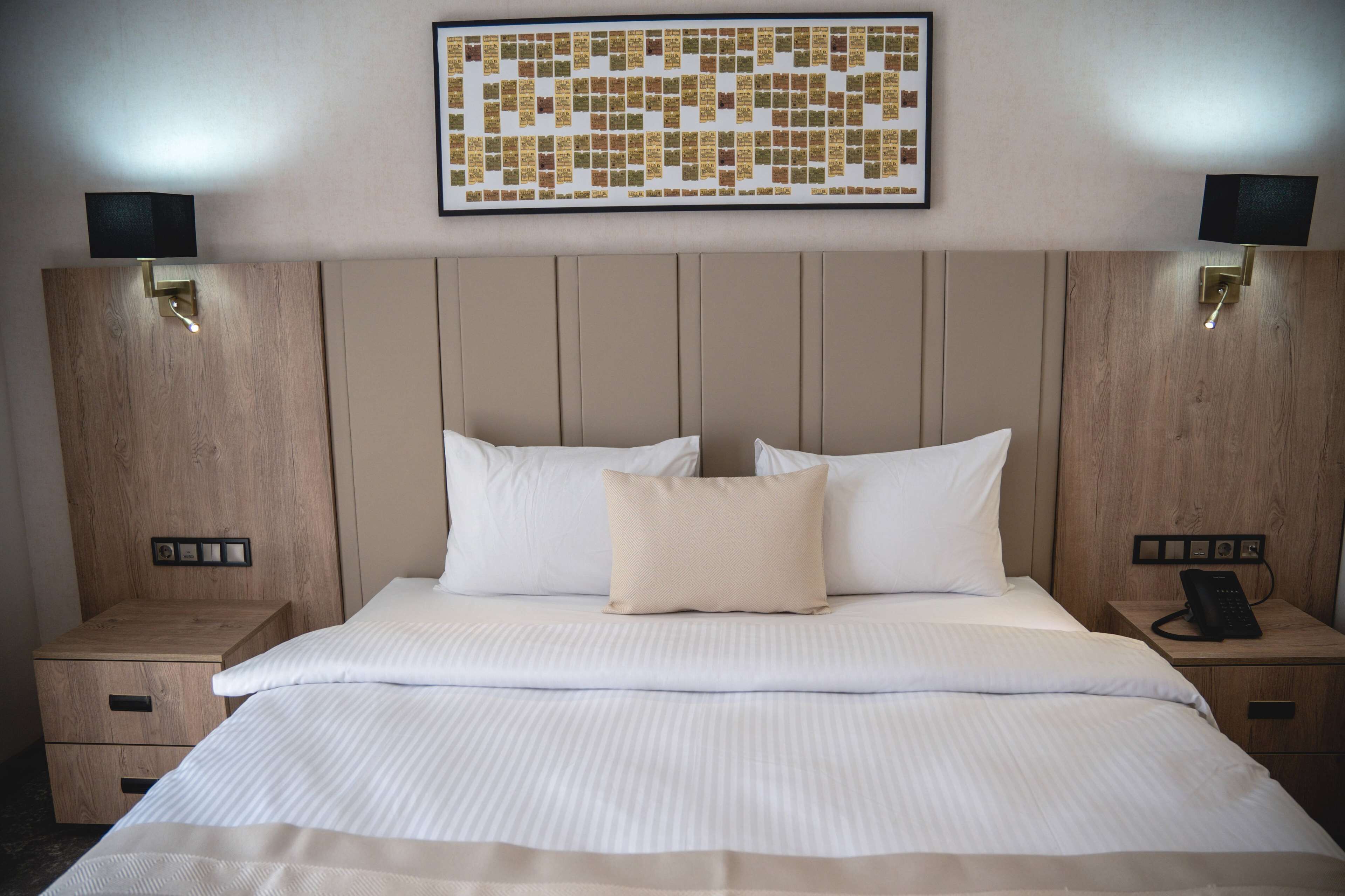 Habitación de hotel con una cama grande, dos mesitas de noche, una obra de arte colgada en la pared y un teléfono sobre una de las mesitas.