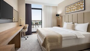 A hotel room with a large bed, a desk, a chair, a flat-screen TV, and a large window with curtains. - Ramada Plaza By Wyndham Batman (Batman)