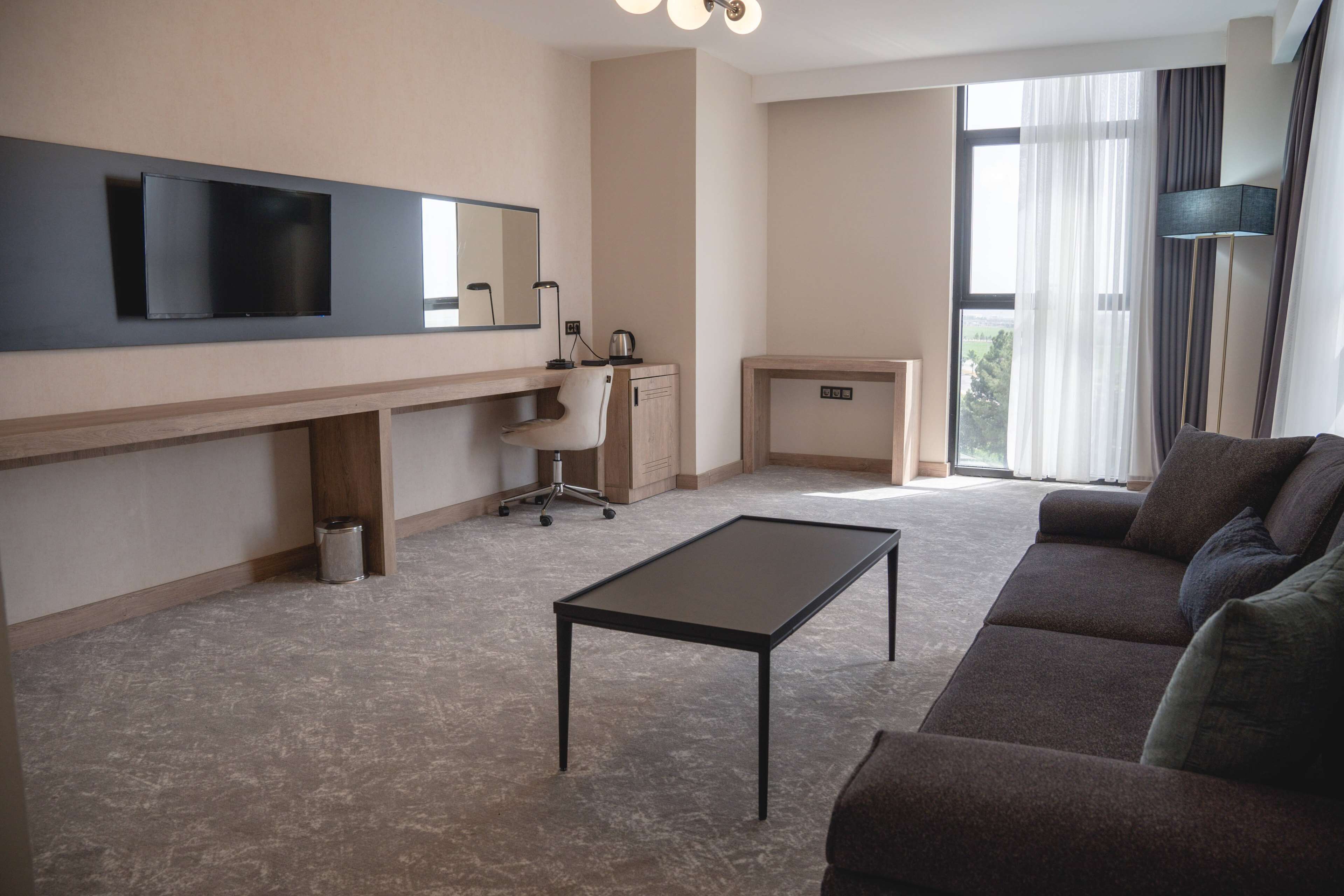A modern living room with a flat-screen TV, a desk, a chair, a sofa, and a coffee machine.
