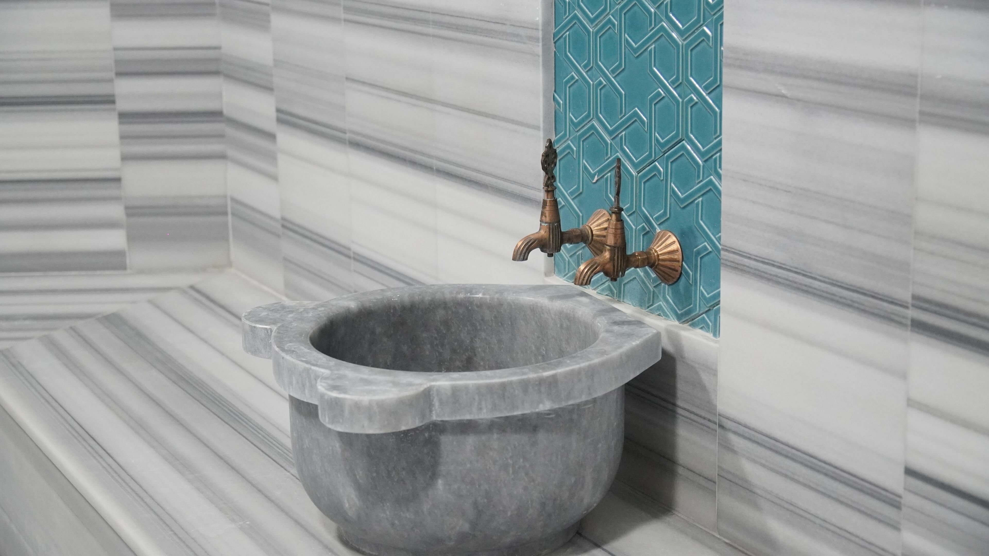 A bathroom with a marble floor, a stone basin, and a blue patterned wall.