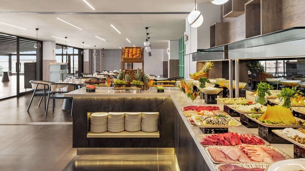 A modern buffet setup with various food items and a seating area with a bench and chairs. - Ramada Plaza By Wyndham Batman (Batman)