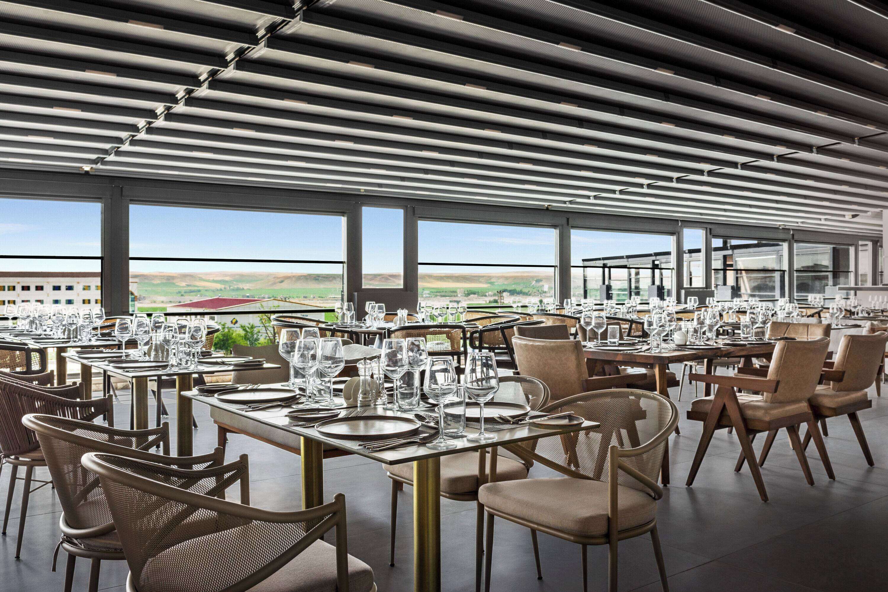 A restaurant with tables set for dining, large windows, and a view of the countryside.