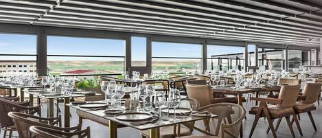 A restaurant with tables set for dining, large windows, and a view of the countryside.
