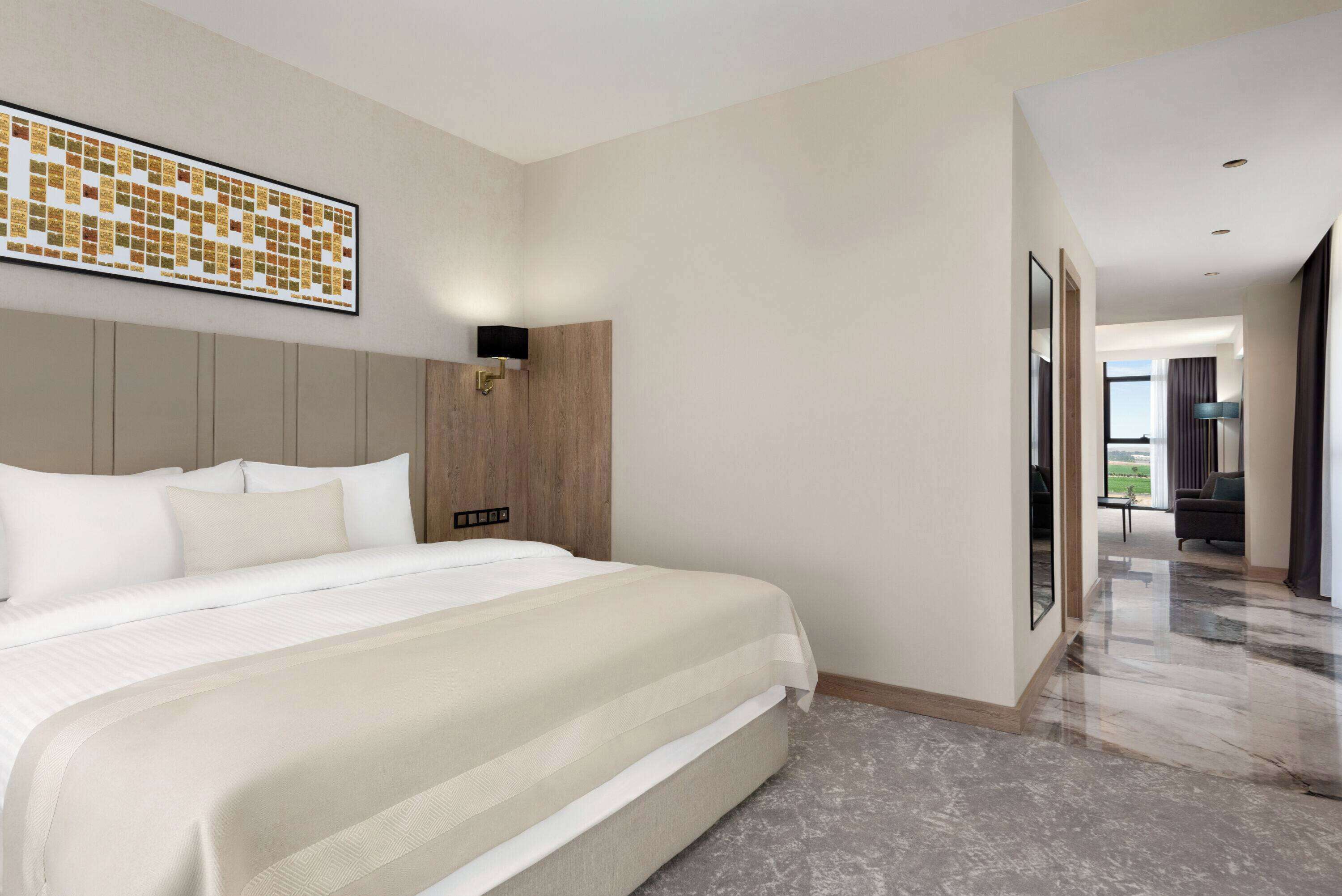 Una camera d'albergo moderna con un letto grande, una testata in legno, un'opera d'arte appesa al muro e vista sull'area esterna tramite una porta di vetro.