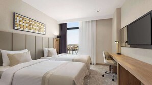 A hotel room with two beds, a desk, a TV, and a view of the outdoors. - Ramada Plaza By Wyndham Batman (Batman)