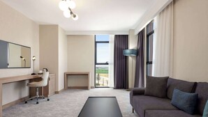 A modern hotel room with a sofa, a desk with a chair, a small table, a large mirror, and a view of the outdoors. - Ramada Plaza By Wyndham Batman (Batman)